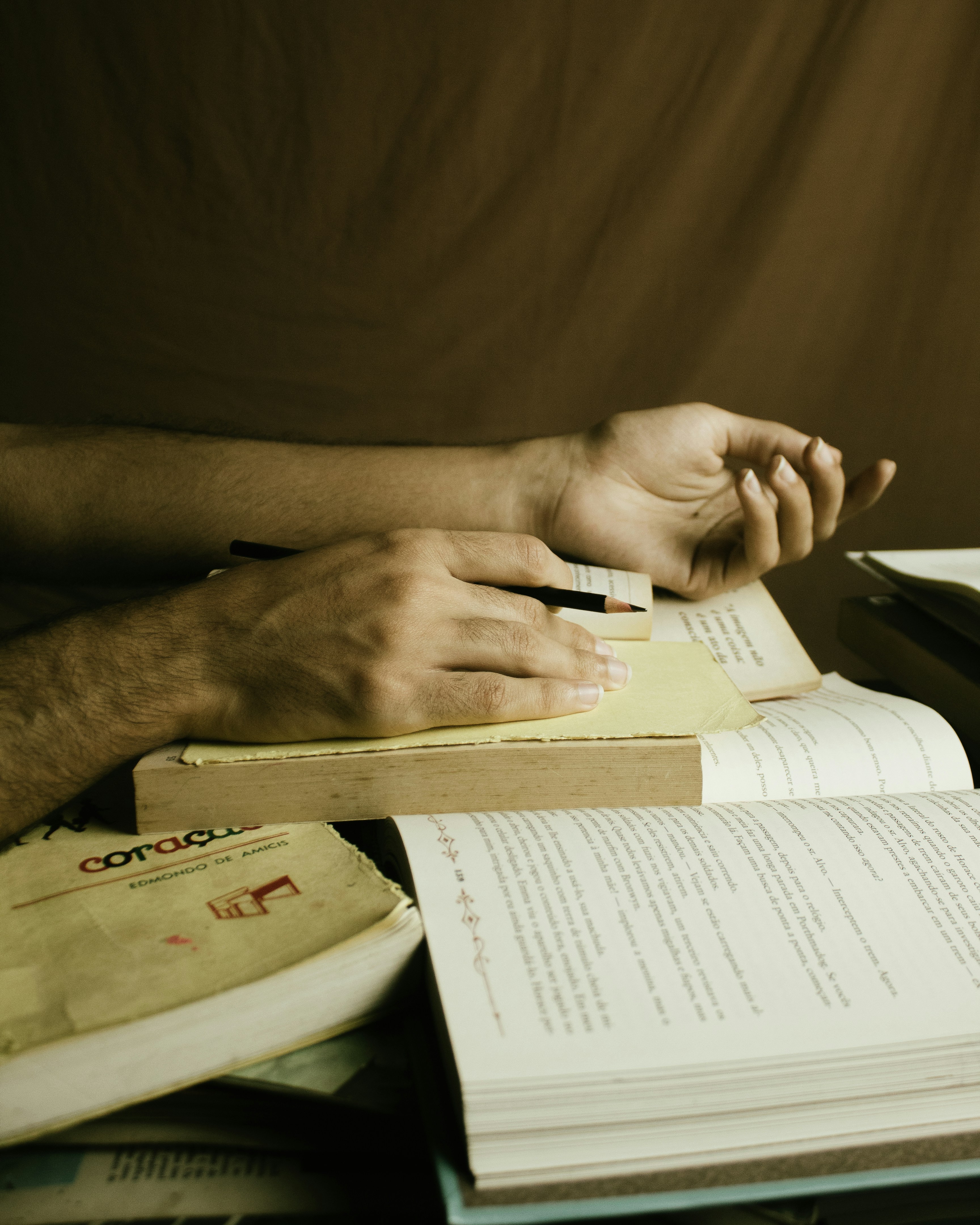 Hands holding a pen over an open notebook with textbooks and notes spread out on a desk
